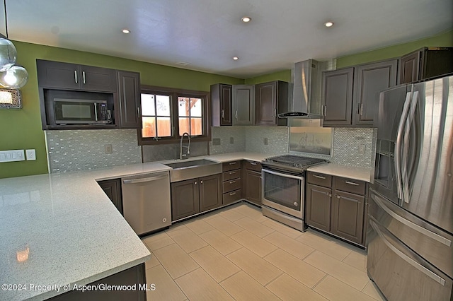 kitchen featuring sink, wall chimney exhaust hood, kitchen peninsula, decorative light fixtures, and appliances with stainless steel finishes