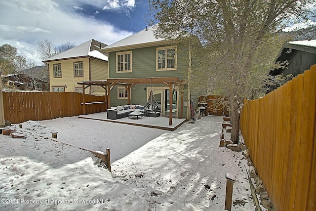 snow covered back of property with an outdoor living space and a pergola