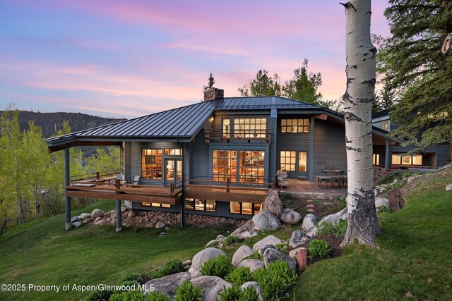 172 Deer Ridge Ln, Snowmass Village, CO 81615 - back of house at dusk with a standing seam roof, a yard, a chimney, metal roof, and a wooden deck