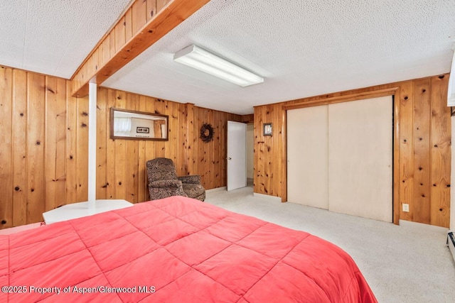 bedroom with carpet flooring, wooden walls, a textured ceiling, and a closet
