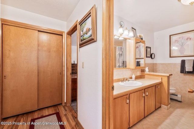 bathroom featuring tile walls, vanity, tile patterned floors, a baseboard heating unit, and toilet