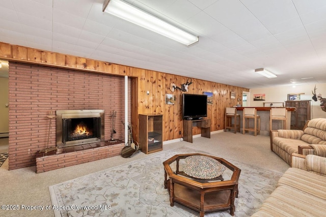 carpeted living area with baseboard heating, a brick fireplace, wood walls, baseboards, and indoor bar