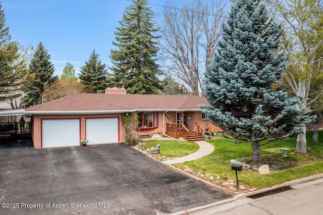 ranch-style house with a chimney, brick siding, aphalt driveway, an attached garage, and a front lawn