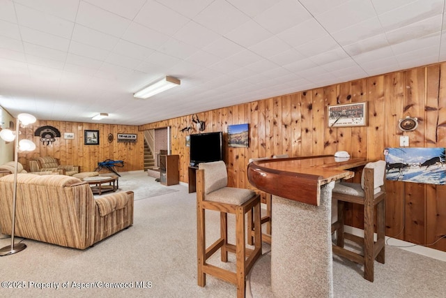 living room featuring stairway, carpet floors, and wooden walls