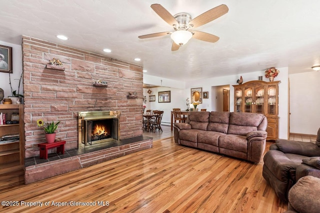 living area featuring baseboards, a fireplace, a ceiling fan, and wood finished floors