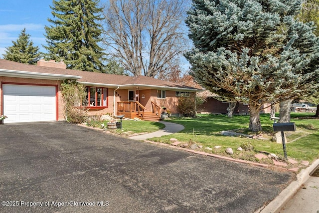 single story home with a front yard, a chimney, brick siding, an attached garage, and driveway