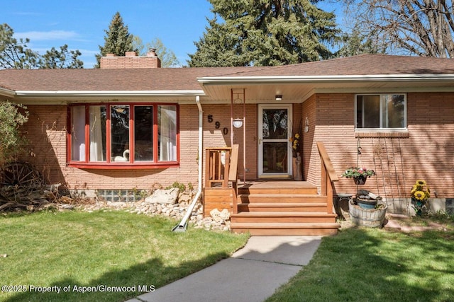view of front of property featuring brick siding, a chimney, a shingled roof, and a front lawn