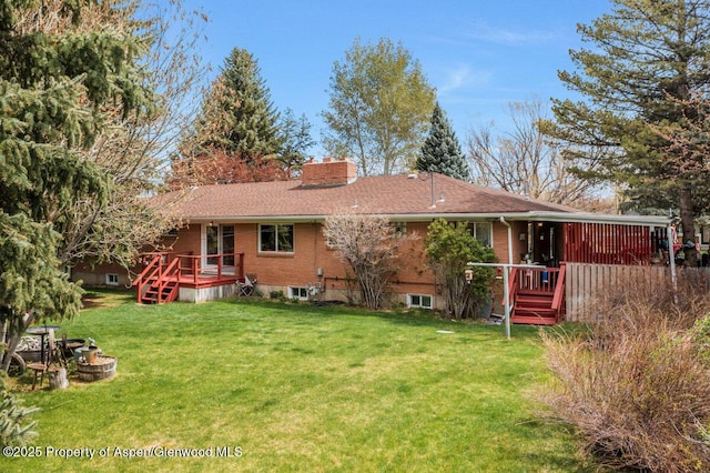 rear view of property featuring a lawn, a wooden deck, a chimney, and brick siding
