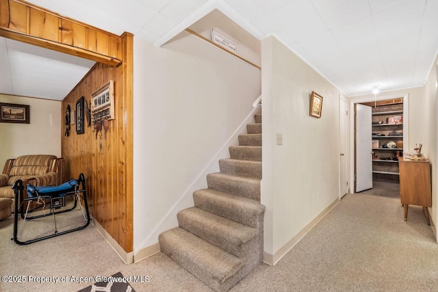 staircase with wooden walls, carpet floors, baseboards, and built in shelves