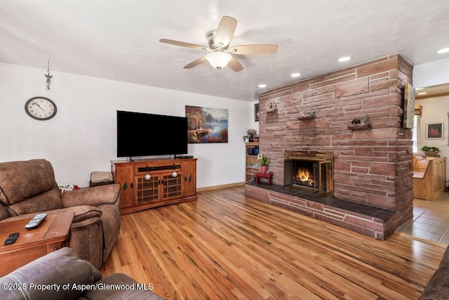 living room with ceiling fan, a stone fireplace, recessed lighting, and wood finished floors