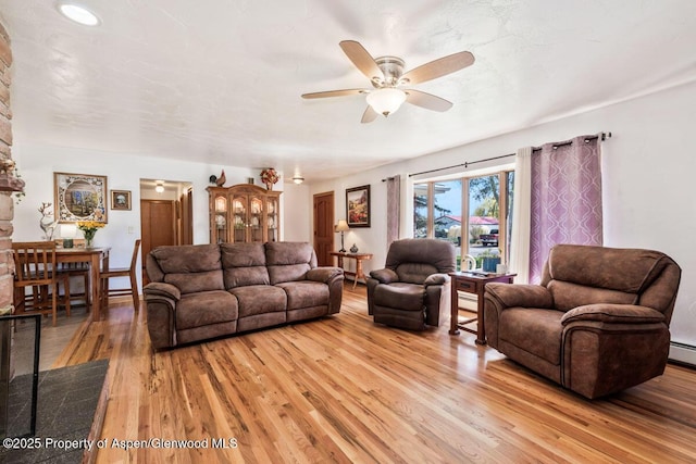 living area featuring light wood-style floors, a ceiling fan, and a baseboard heating unit