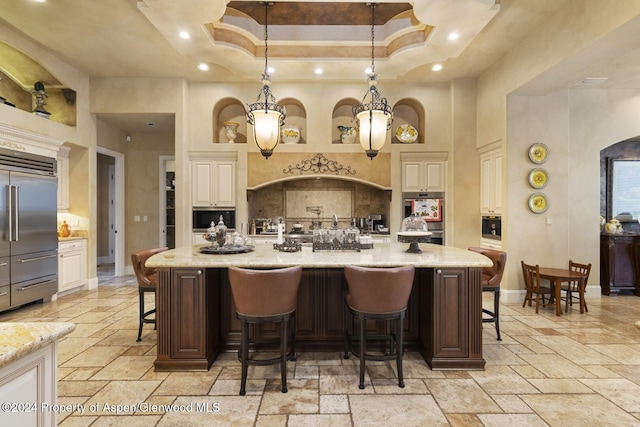 kitchen featuring a large island with sink, stainless steel built in fridge, hanging light fixtures, and a breakfast bar area