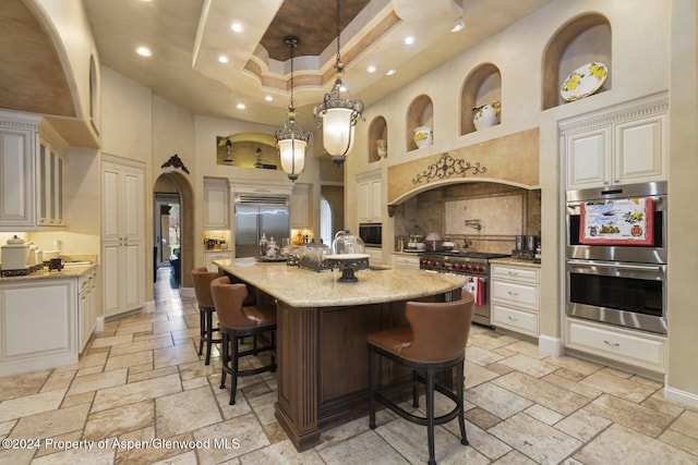 kitchen with light stone countertops, a kitchen bar, a towering ceiling, a kitchen island with sink, and high quality appliances