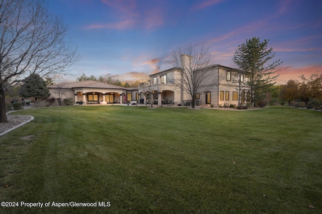 back house at dusk featuring a lawn