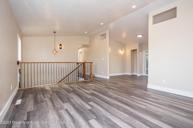 empty room featuring wood-type flooring, vaulted ceiling, and a textured ceiling