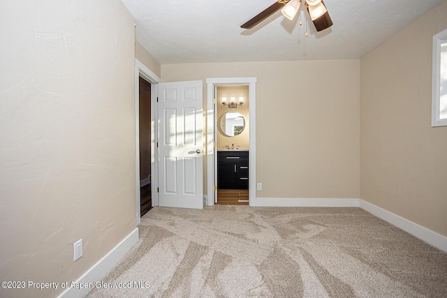 unfurnished bedroom featuring ceiling fan, ensuite bathroom, sink, and carpet floors