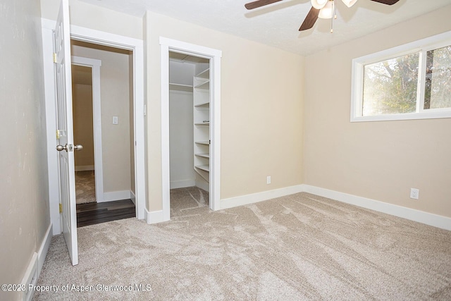 unfurnished bedroom featuring a spacious closet, light colored carpet, a closet, and ceiling fan