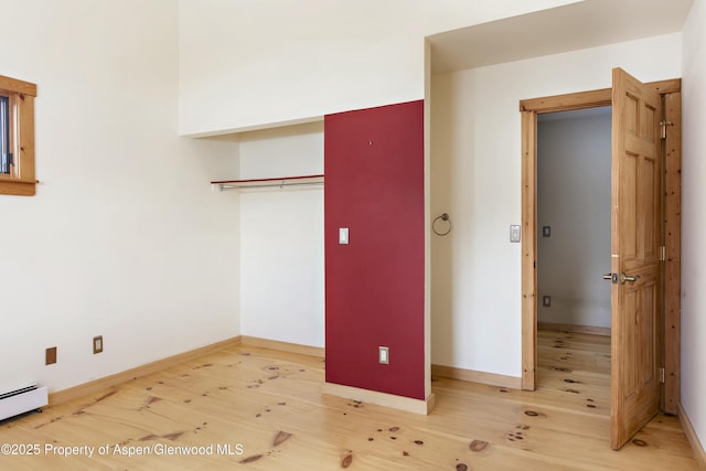 unfurnished bedroom with hardwood / wood-style flooring, a baseboard radiator, and a closet