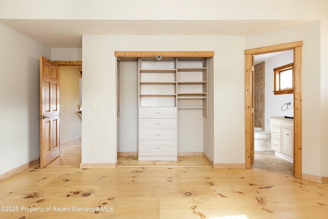 unfurnished bedroom with ensuite bath, light wood-type flooring, and a closet