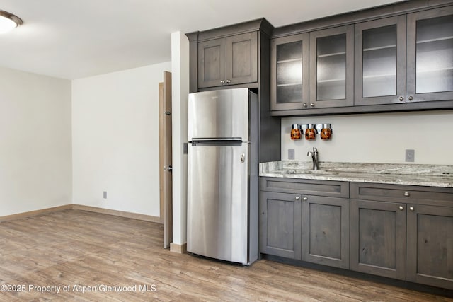 kitchen with dark brown cabinetry, stainless steel fridge, light stone countertops, and sink