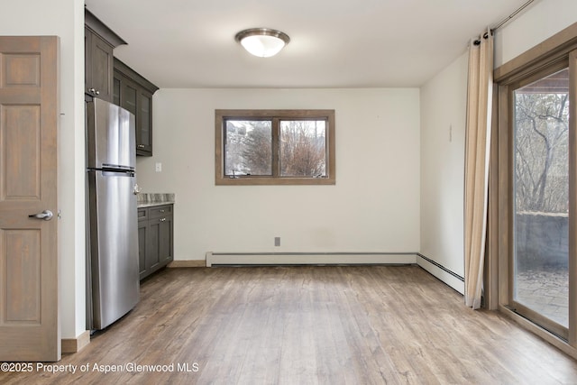 kitchen with dark brown cabinetry, a baseboard heating unit, stainless steel refrigerator, and light hardwood / wood-style floors