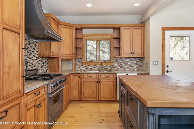 kitchen featuring wall chimney range hood, stainless steel stove, light hardwood / wood-style flooring, sink, and backsplash