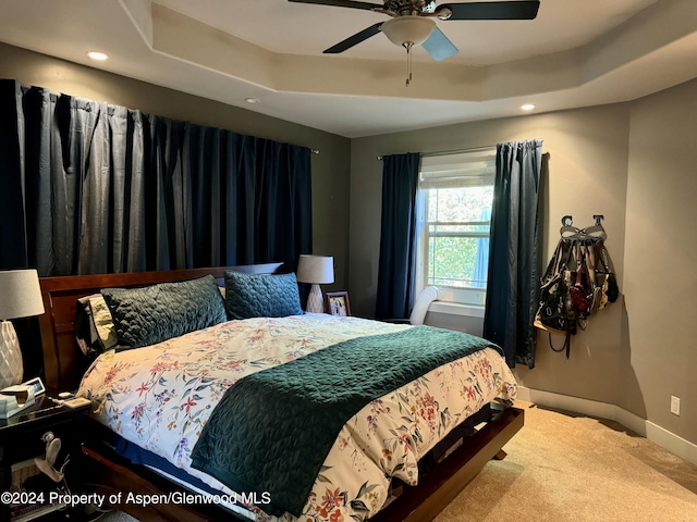 carpeted bedroom with a raised ceiling and ceiling fan