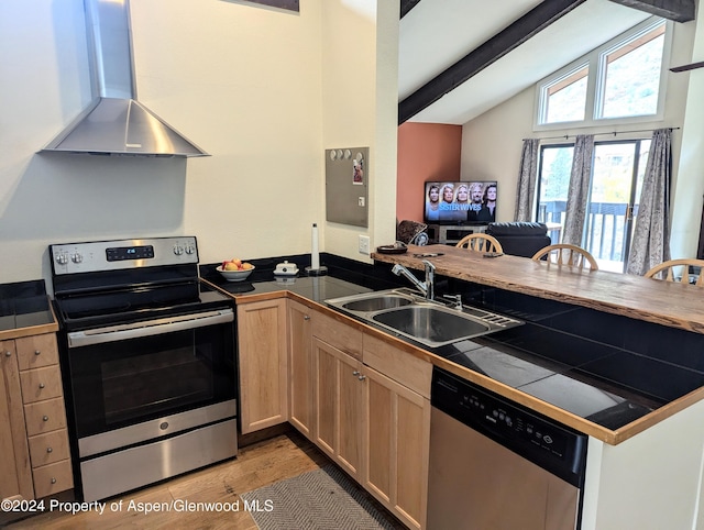 kitchen with tile counters, sink, wall chimney range hood, lofted ceiling with beams, and appliances with stainless steel finishes