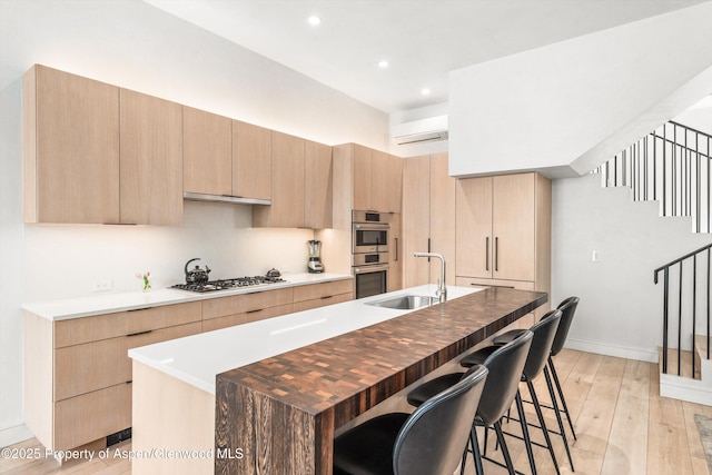 155 Lone Pine Rd Unit 2, Aspen, CO 81611 - kitchen featuring a wall mounted air conditioner, light brown cabinetry, stainless steel appliances, light wood-style floors, and a breakfast bar