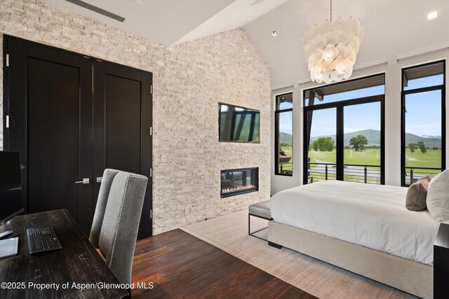 295 Aspen Valley Ranch Rd, Woody Creek, CO 81656 - bedroom featuring wood finished floors, vaulted ceiling, access to outside, a glass covered fireplace, and a chandelier