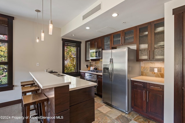 kitchen with backsplash, hanging light fixtures, sink, appliances with stainless steel finishes, and a breakfast bar area