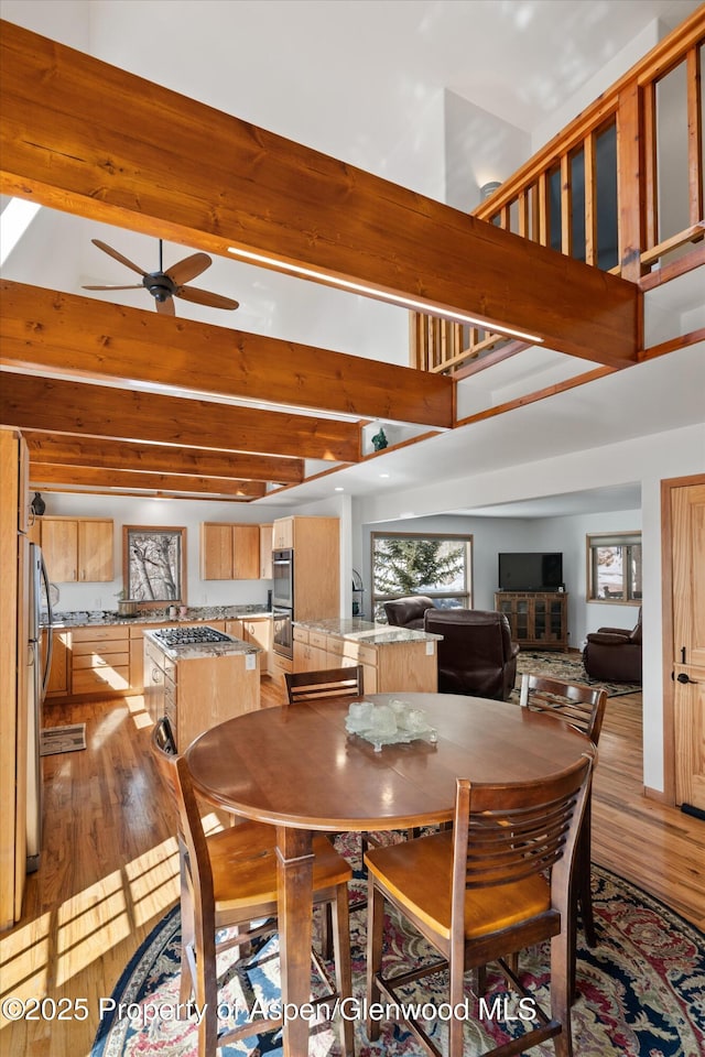 dining area with ceiling fan, light wood-style flooring, a towering ceiling, and beam ceiling