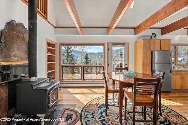 dining room with light wood-style floors, a baseboard radiator, a wood stove, and a healthy amount of sunlight