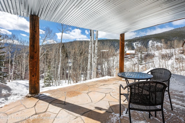 snow covered patio featuring a mountain view and a wooded view