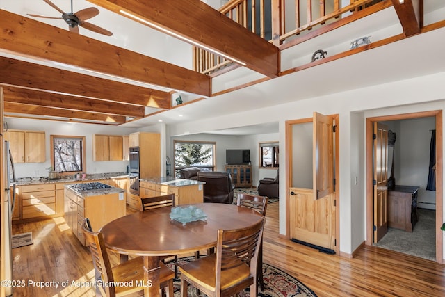 dining room featuring light wood-style floors, beamed ceiling, and a towering ceiling