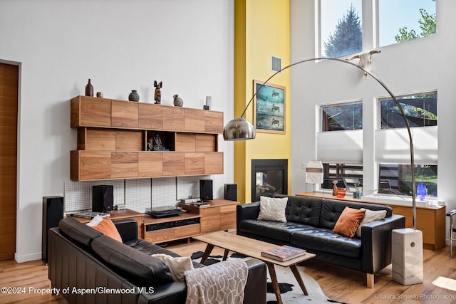 living room with a tiled fireplace, light hardwood / wood-style flooring, and a towering ceiling