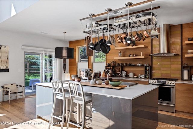 kitchen with wall chimney exhaust hood, light wood-type flooring, stainless steel range, decorative light fixtures, and a kitchen island