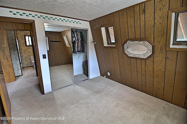 unfurnished bedroom with wood walls, light carpet, and a closet