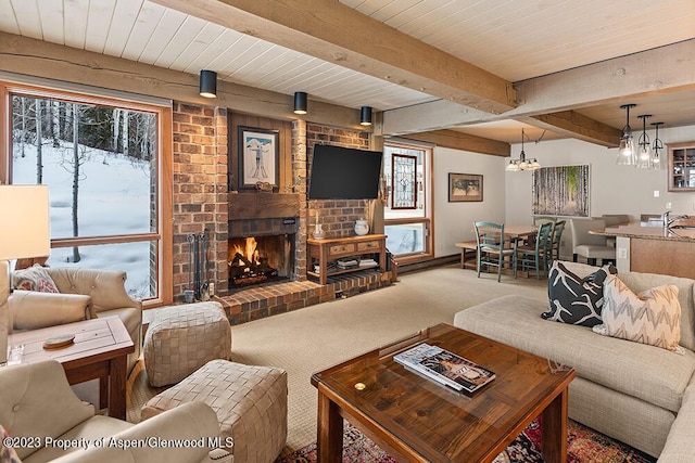 carpeted living room featuring beam ceiling, a brick fireplace, and a notable chandelier