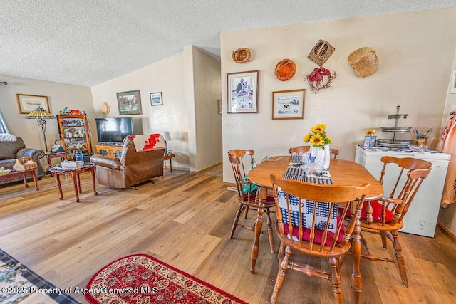 dining room with lofted ceiling, a textured ceiling, and light wood-style flooring