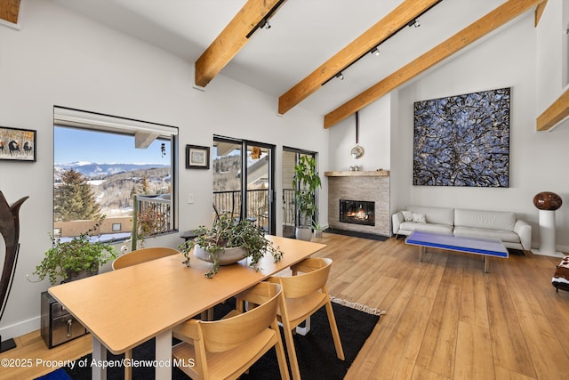 dining area with track lighting, a brick fireplace, vaulted ceiling with beams, light wood-type flooring, and a mountain view