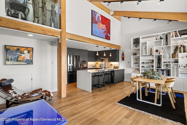 dining area with rail lighting, a high ceiling, beam ceiling, light hardwood / wood-style flooring, and sink