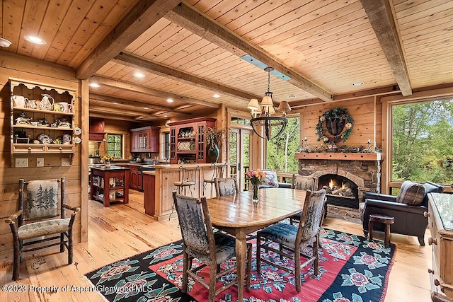 dining room featuring beam ceiling, a stone fireplace, light hardwood / wood-style flooring, wooden walls, and wood ceiling