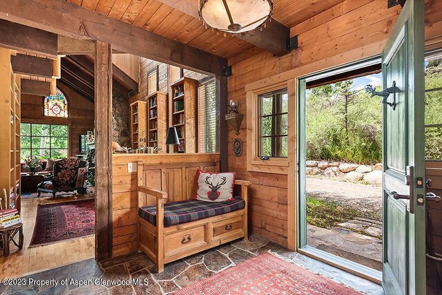 mudroom with vaulted ceiling with beams, wooden walls, and wood ceiling