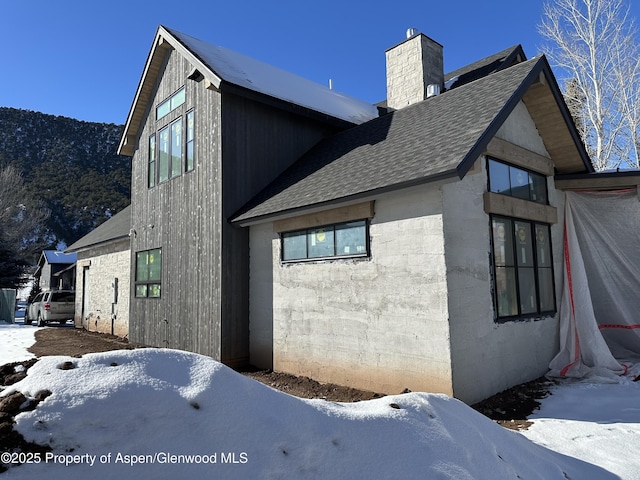 snow covered property with a shingled roof and a chimney