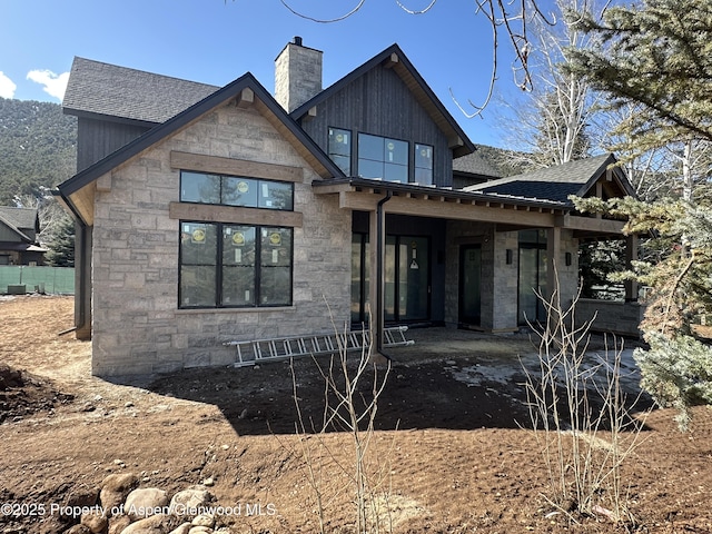 back of property featuring stone siding, a chimney, and roof with shingles