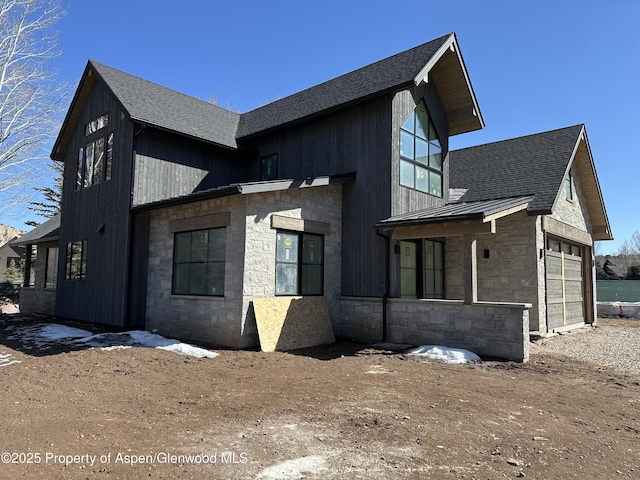 view of side of home featuring a garage, a shingled roof, stone siding, metal roof, and a standing seam roof