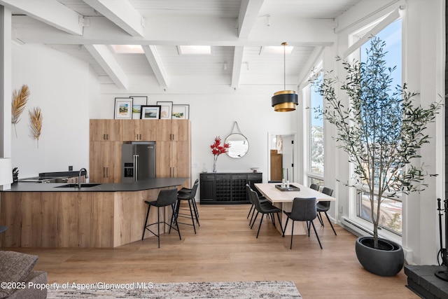 kitchen with pendant lighting, a breakfast bar, sink, beam ceiling, and stainless steel fridge with ice dispenser