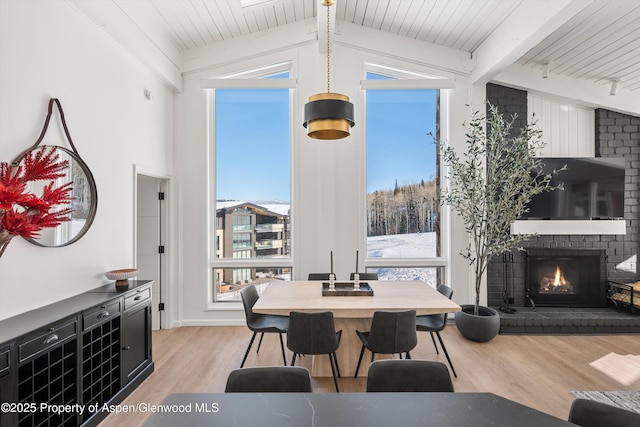 dining area featuring a fireplace, lofted ceiling with beams, light hardwood / wood-style floors, and wooden ceiling