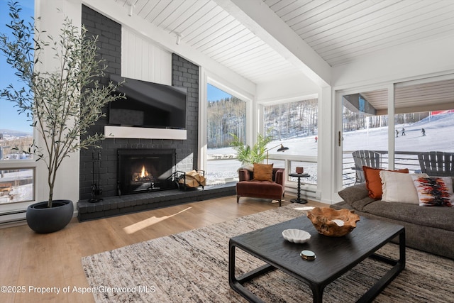 interior space featuring beam ceiling, a brick fireplace, plenty of natural light, and hardwood / wood-style flooring